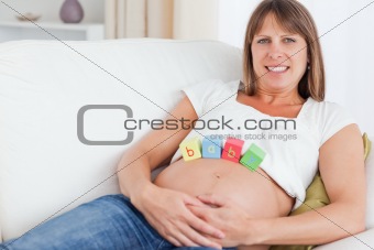 Pretty pregnant woman playing with wooden blocks while lying on 