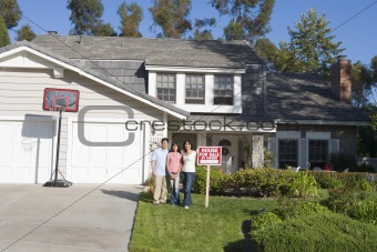 Family Standing Outside House With Real Estate Sign