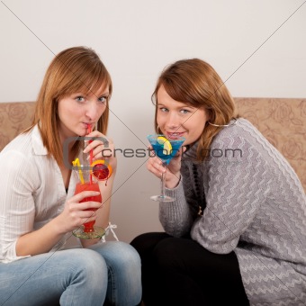 Two pretty friends celebrating with colorful cocktails on white background