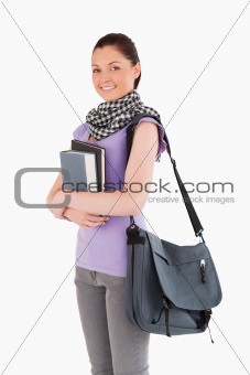 Beautiful student holding books and her bag while standing