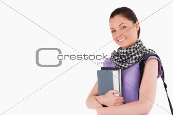 Good looking student holding books and her bag while standing