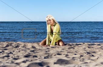 blonde girl in a yellow tunic, sits near the sea on his knees