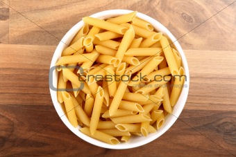 Top view of dry penne rigate in white ceramic bowl on wooden floor