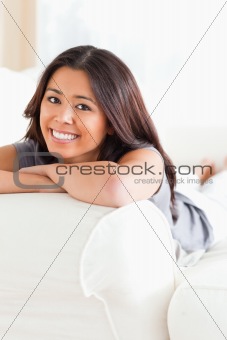 smiling woman lying on sofa with crossed arms looking into camer