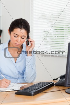 Lovely woman using her mobile phone while writing