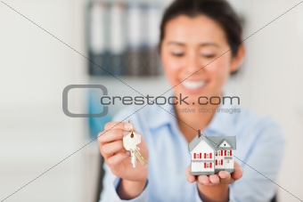 Charming woman holding keys and a miniature house while looking 