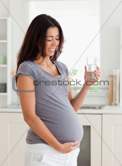 Charming pregnant woman holding a glass of water while standing