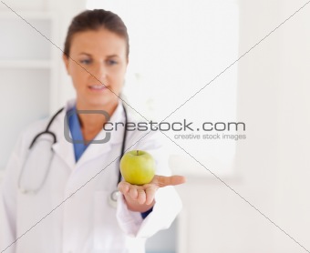 Good looking brunette doctor with stethoscope looking at an apple