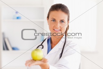 Doctor with stethoscope holding an apple looking into the camera