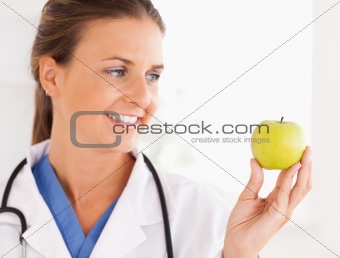 Close up of a smiling doctor with stethoscope looking at an apple