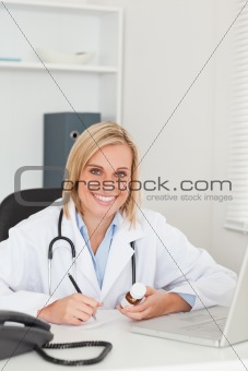 Doctor writing something down while holding medicine looks into 