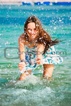 Beautiful young girl splashing the water in the sea