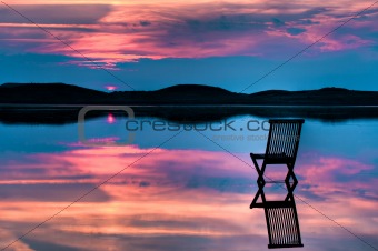 Chair in calm water with sunset