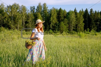 Girl with a basket is on the meadow