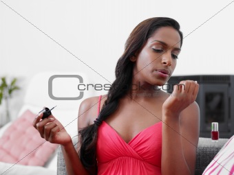 woman applying red nail varnish on sofa