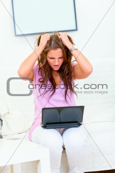 Stressed modern housewife sitting on sofa with laptop
