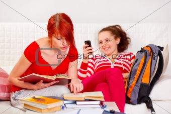 Responsible girl studying while her girlfriend reading sms

