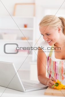 Close up of a blonde woman using a laptop slicing a pepper