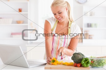 Close up of a blonde woman using a notebook slicing a pepper