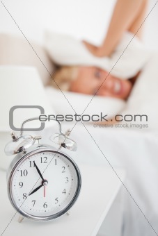 Portrait of a woman hidding her head in a pillow while the alarmclock is ringing