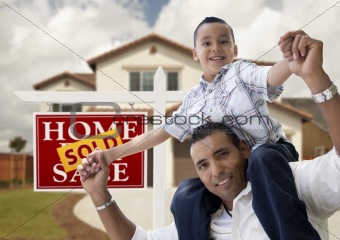 Happy Hispanic Father and Son in Front of New House and Sold Real Estate Sign.