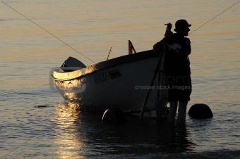 The fisherman near a boat during sunset
