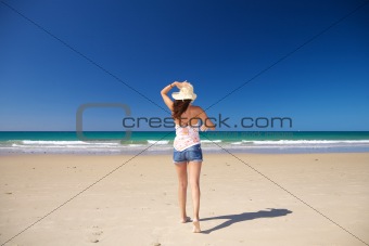 walking holding on straw hat at beach