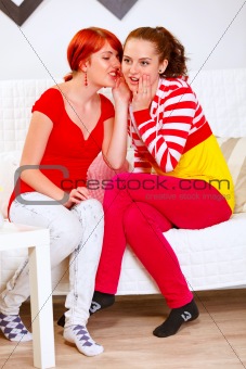 Pretty girl whispering gossips in ear of her interested girlfriend

