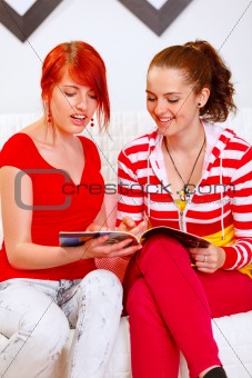 Cheerful girlfriends sitting on sofa and looking fashion magazine
