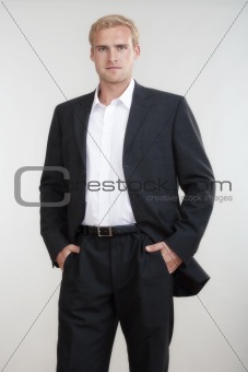 portrait of a young businessman with blond hair in suit standing - isolated on light gray