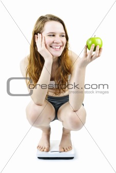 Young smiling girl on bathroom scale holding apple