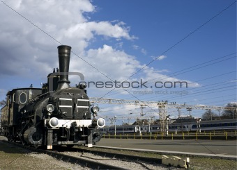 Old rusty locomotive with new powerful trains in the background.
