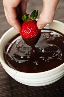 Hand dipping strawberry in chocolate