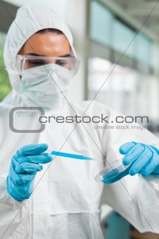 Portrait of a protected female science student dropping blue liquid in a Petri dish