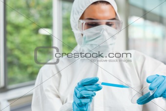 Protected female science student dropping blue liquid in a Petri dish