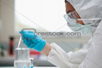 Close up of a protected female scientist dropping liquid in a test tube