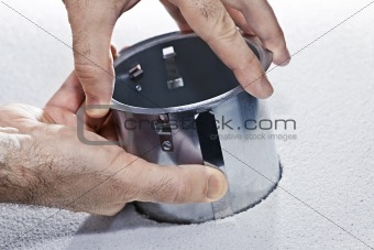 Hands installing metal pot light fixture