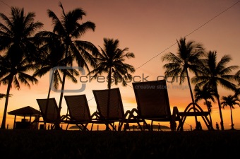 Row deckchairs on beach at sunset,