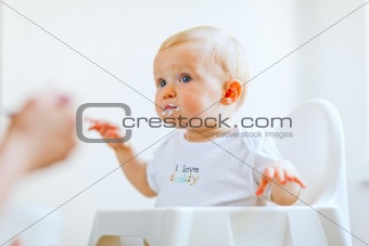 Eat smeared lovely baby in baby chair feeding by mother
