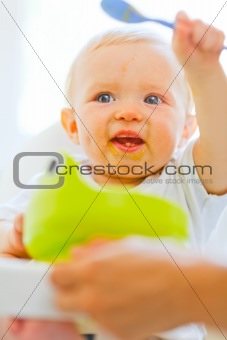 Eat smeared adorable baby girl in baby chair playing with spoon
