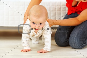 Mother helping cheerful baby learn to creep
