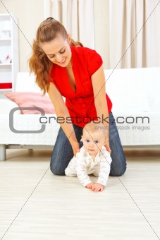 Smiling mother helping cheerful baby learn to creep
