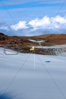 cold snow covered links golf course with yellow flag