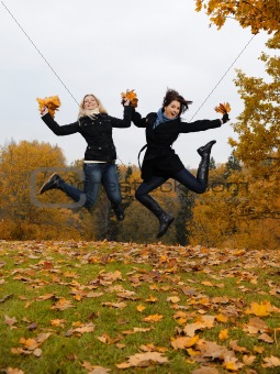 two beautiful girl friends with autumn leafs in a park jumping