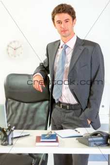 Portrait of confident modern businessman standing at office desk
