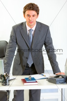 Portrait of confident modern businessman holding hands on office desk
