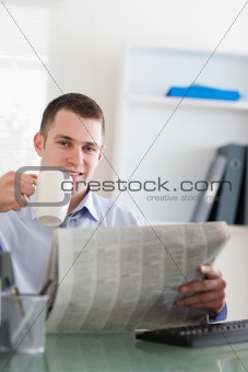 Smiling businessman reading the newspaper and having a coffee