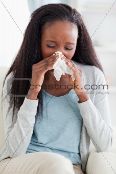 Close up of woman blowing her nose on sofa