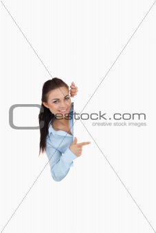 Smiling businesswoman looking around the corner while pointing