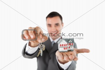 Close up of keys and miniature house being held by male estate agent